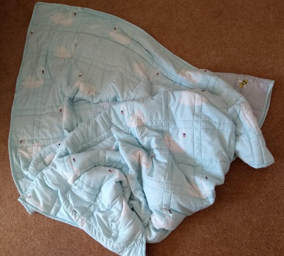 A pale blue weighted blanket, with swans on one side and bees on the other.