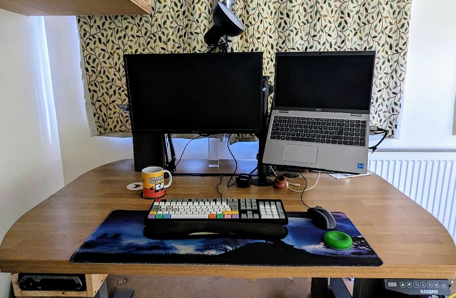 A wide desk with a monitor, laptop, keyboard, mouse and wrist rests.
