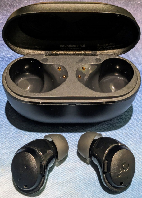 The open case is at the top of the photo - an oval shape with two recesses (one for each ear bud).  The earbuds are removed and in front of the case, with the grey rubber "cushions" that go inside the ear pointing towards the case.  Both the case and the earbuds are black.