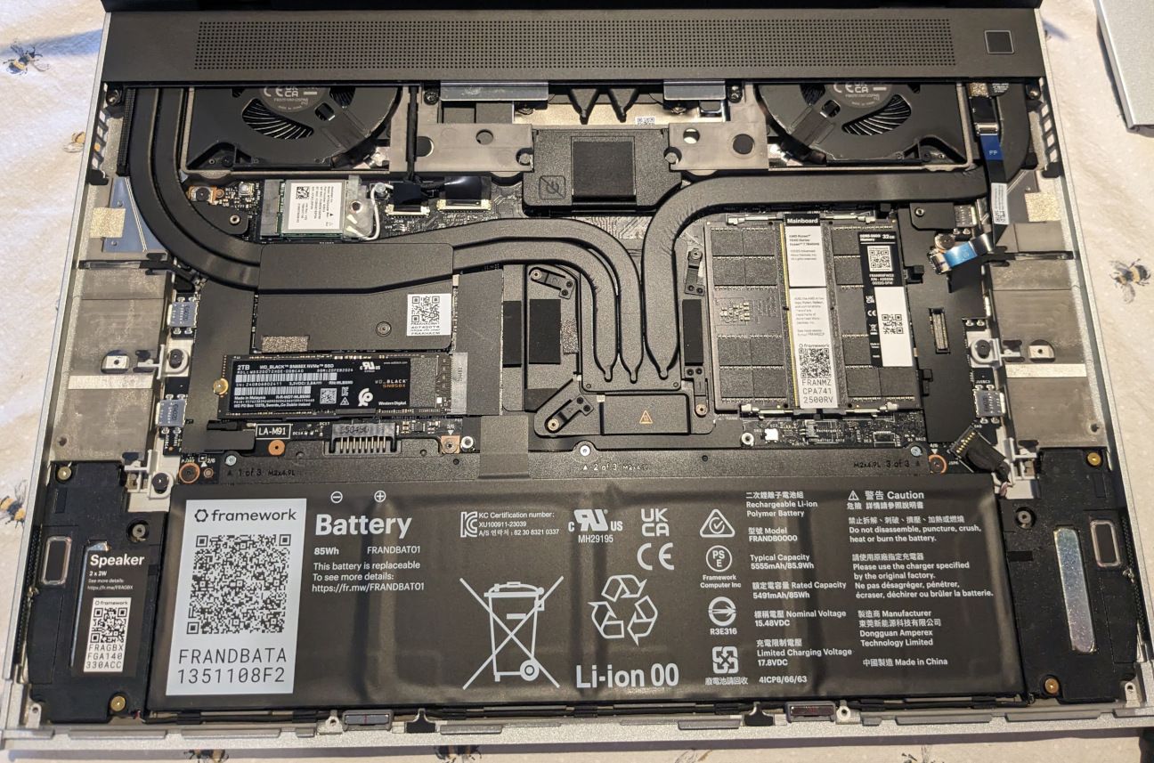 Photograph of inside the laptop.  All components are labelled, with the battery in the foreground.  The majority of the components are black.