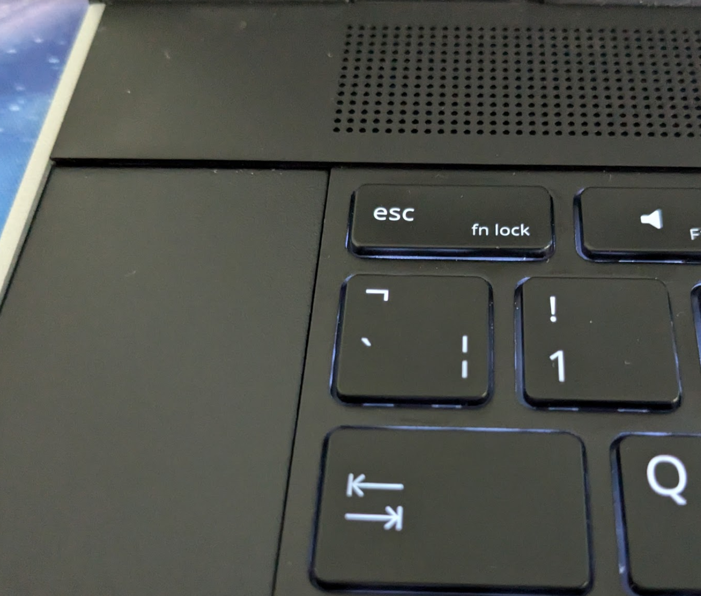 Photo showing the left edge of a laptop keyboard.  To the left of the keyboard is a smooth black spacer, which has a pronounced step up above it.