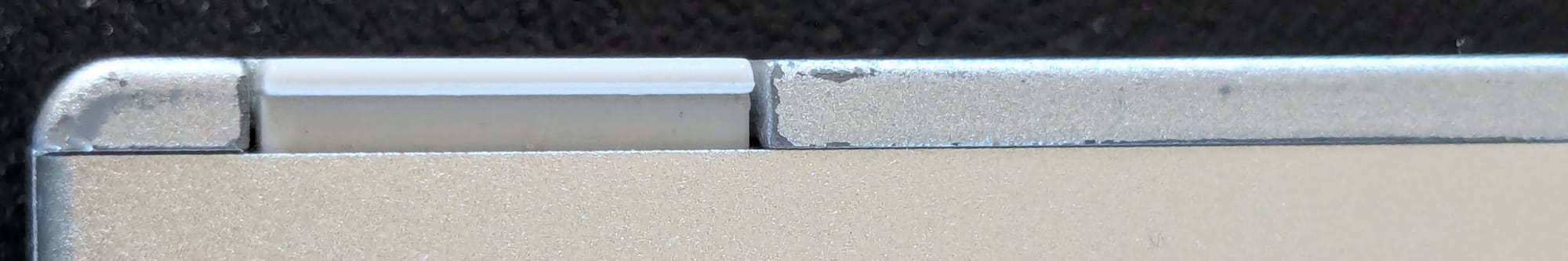 Photograph showing the edge of a laptop. The colour should be a completely silver on the plastic edge, but the paintwork has started to wear off resulting in grey plastic showing in places.